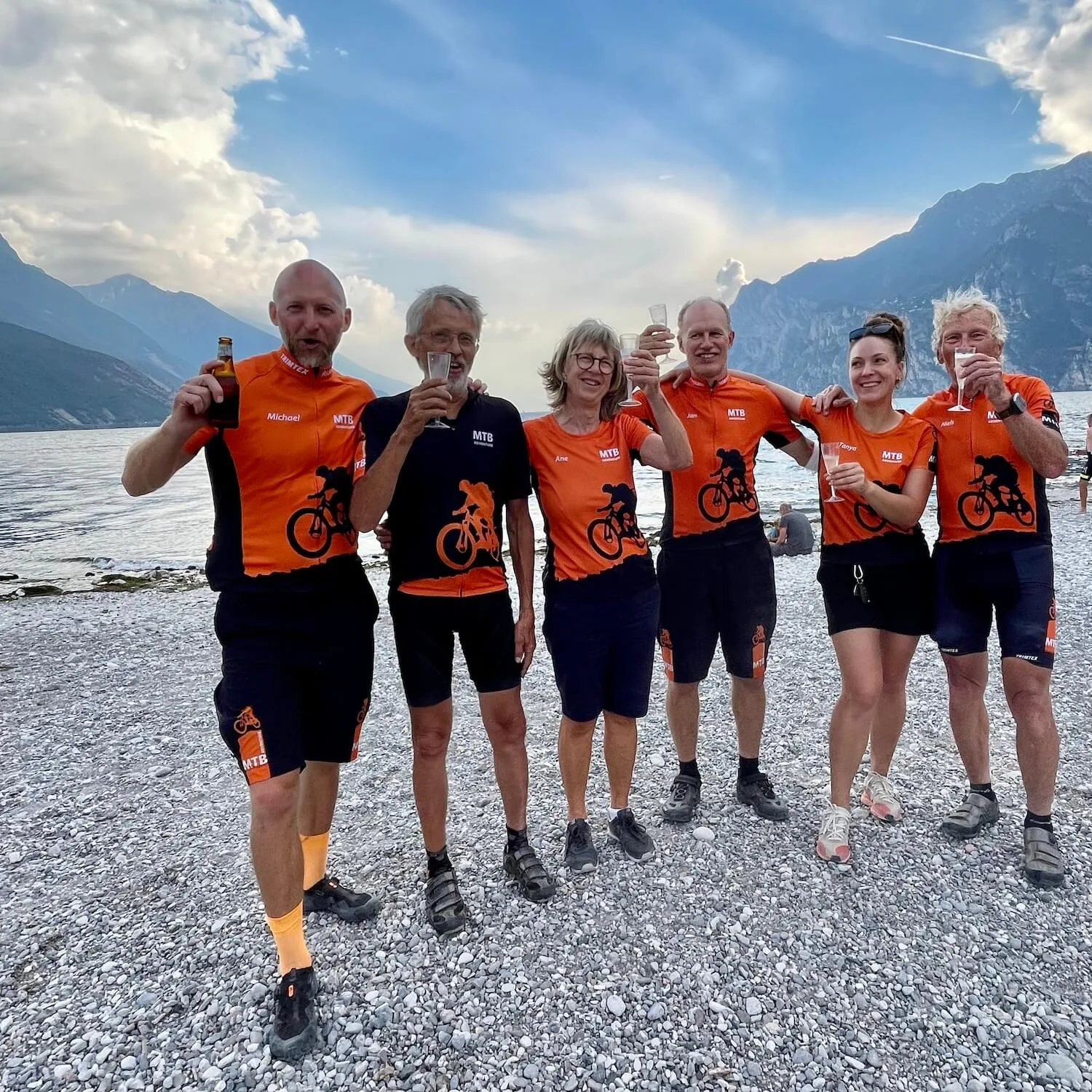 A small Gravel Adventure group raising a toast on the shore of Lake Garda at the end of a Trans Alp gravel tour
