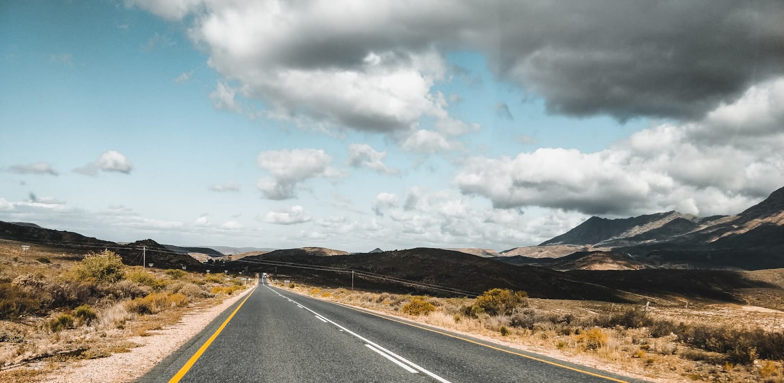 Lone gravel cyclist riding towards distant mountains across red earth plains under vast African sky