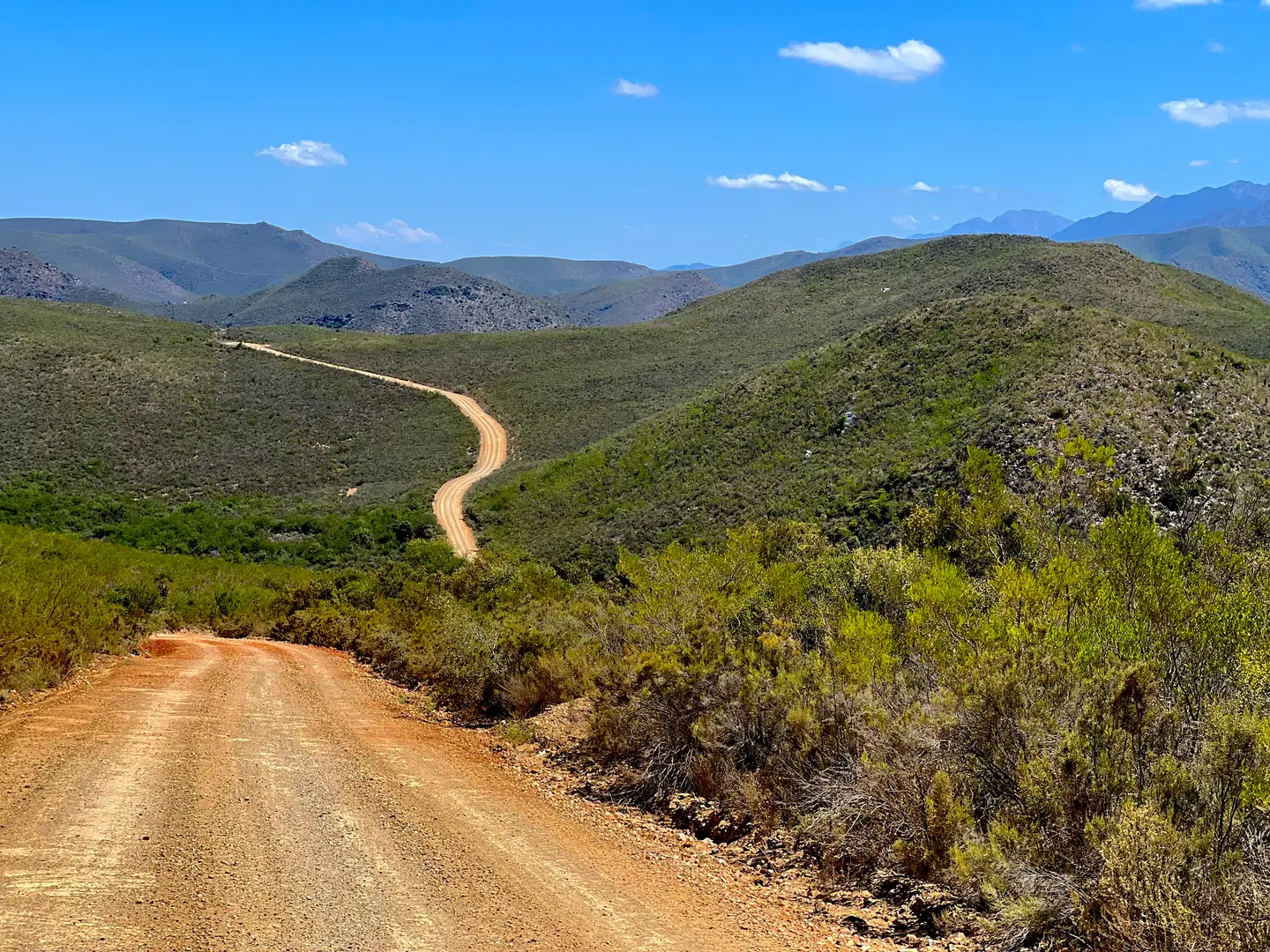 Red gravel road winding over green hills under a blue sky in the Western Cape