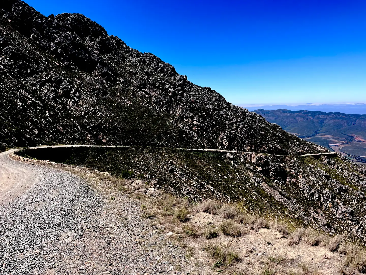 Gravel road cut across a steep rocky mountainside above a valley